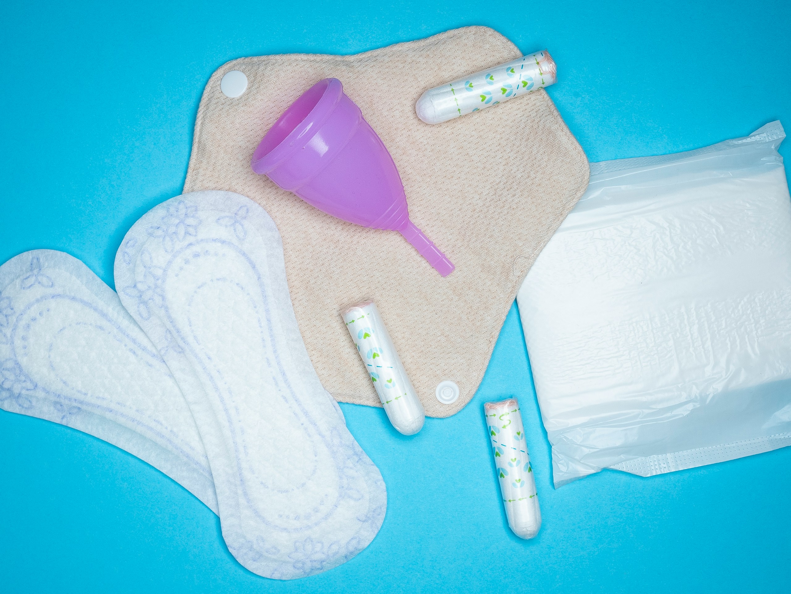 Menstrual products and supplies (pads, tampons, menstrual cups) on a colorful background.